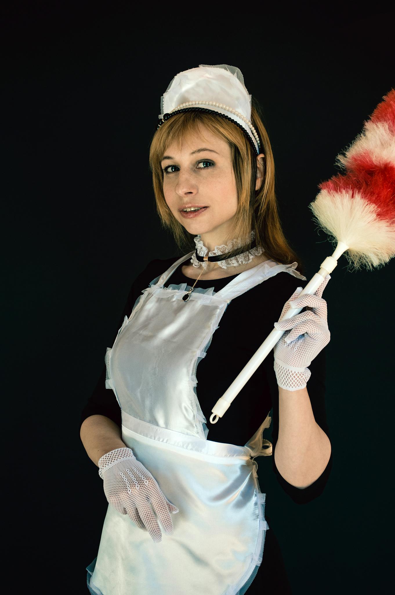 Smiling young woman in a classic maid outfit holding a feather duster for cleaning.